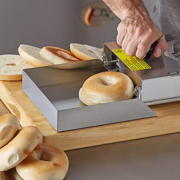 A person using a Prince Castle bagel tray to slice a bagel on a counter.
