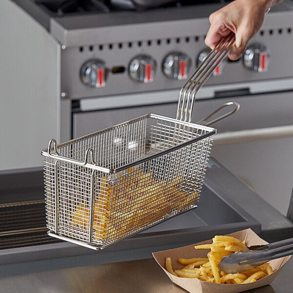 A hand holding a Prince Castle fry basket with French fries in it over a fryer.