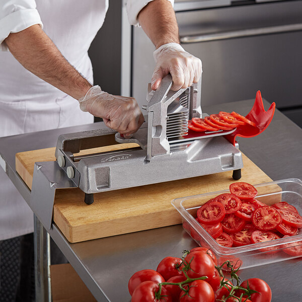 A person using a Prince Castle Tomato Saber machine to slice tomatoes on a cutting board.