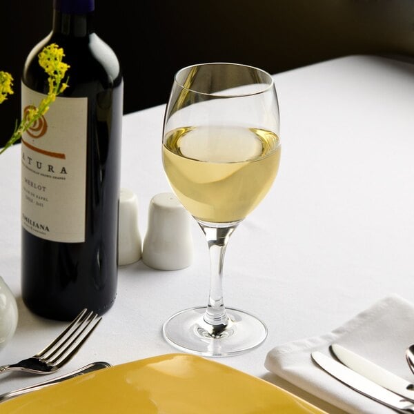A Stolzle Nadine all-purpose wine glass filled with white wine on a table next to a bottle of wine.