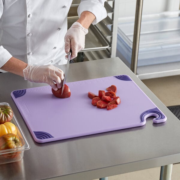 A chef cutting tomatoes on a purple San Jamar cutting board.