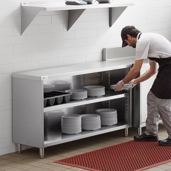 A man in a black apron putting plates in a Regency stainless steel dish cabinet.