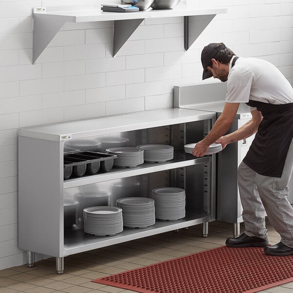 A man wearing a black apron putting plates in a Regency stainless steel dish cabinet.