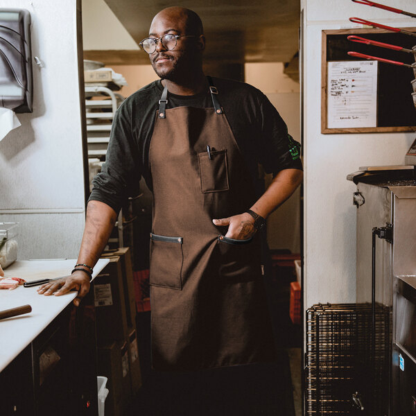 A man wearing a Hardmill brown canvas bib apron.