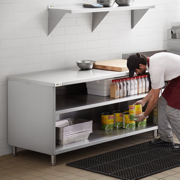 A man in a professional kitchen using a Regency stainless steel table with adjustable midshelf to store food.
