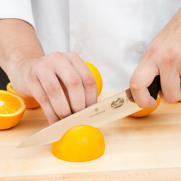 A chef using a Victorinox Chef Knife to cut an orange.