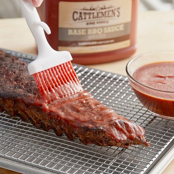 A hand brushing Cattlemen's BBQ sauce on a rack of ribs.