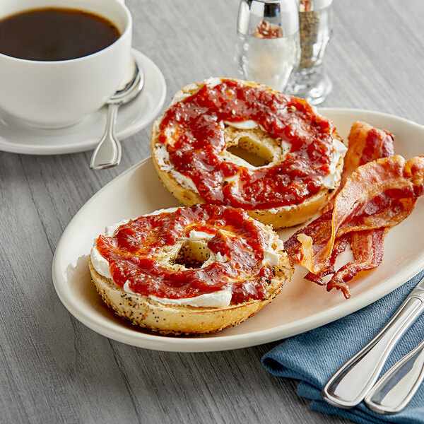 A plate with a bagel topped with TBJ Gourmet Savory Tomato Jam and bacon.