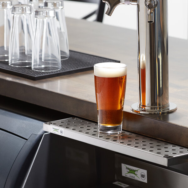 A glass of beer on a Regency stainless steel beer drip tray on a counter.