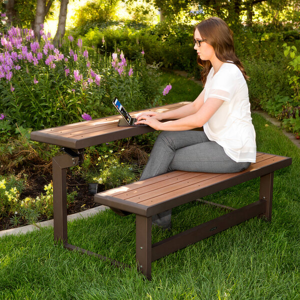 A woman sitting on a Lifetime brown convertible bench typing on a laptop.