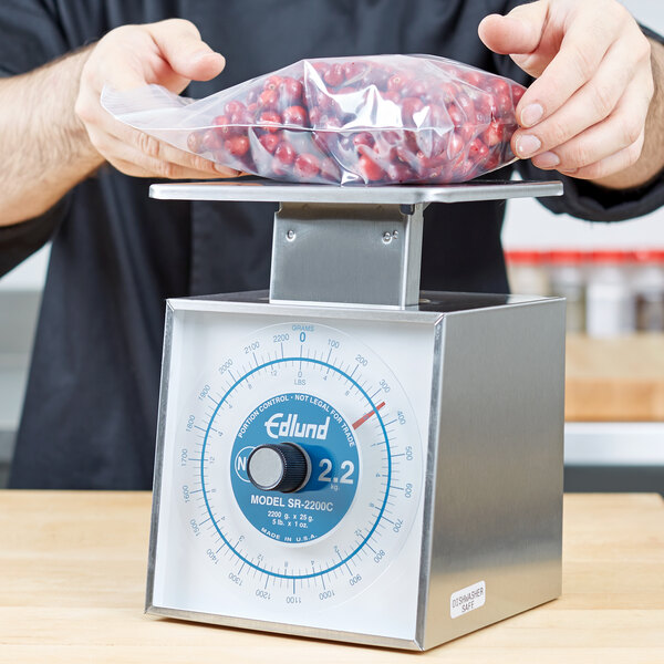 A person weighing a bag of red beans on an Edlund mechanical portion scale on a table.