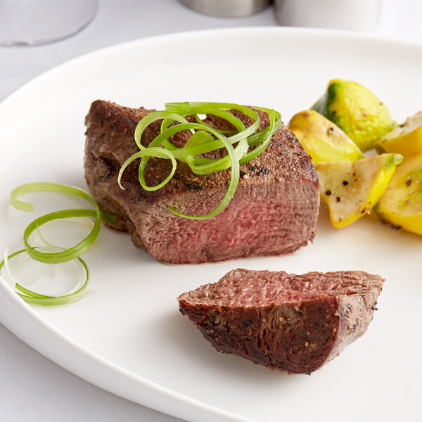 A Warrington Farm Meats filet mignon steak on a white plate with green onions.