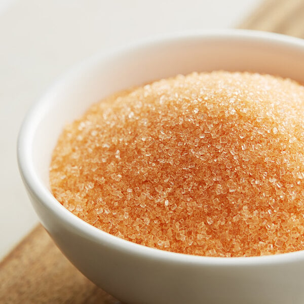 A bowl of orange sanding sugar on a wooden table.