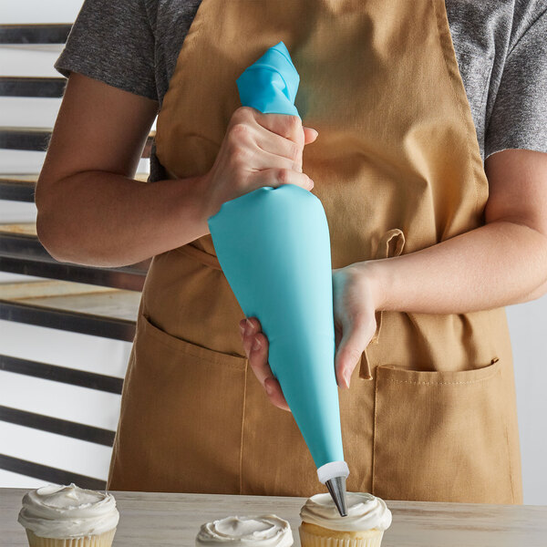A person in an apron using a blue thermoplastic polyurethane pastry bag to decorate cupcakes.