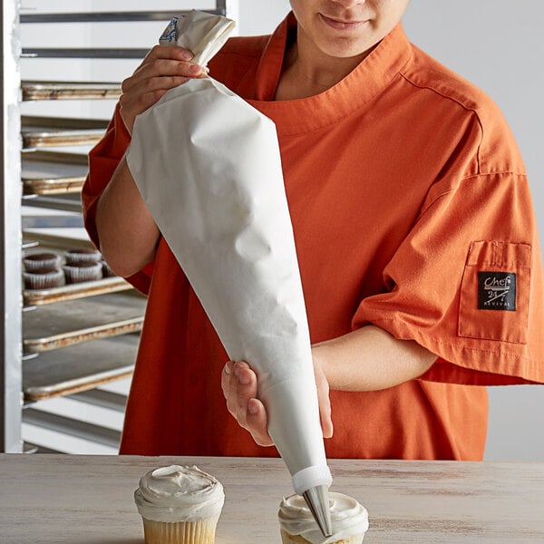 A woman in an orange shirt holding a white Ateco Wunderbag full of frosting.