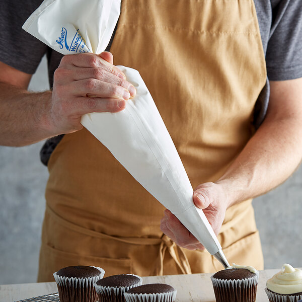 A person using an Ateco polyurethane coated cotton pastry bag to pipe white frosting onto a cupcake.