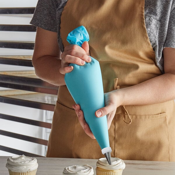 A person in an apron using a blue thermoplastic pastry bag to decorate cupcakes.