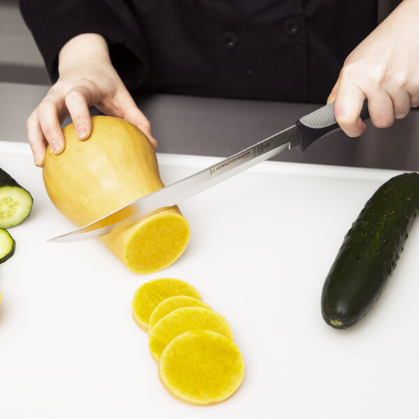 A person using a Dexter-Russell V-Lo Scalloped Utility Knife to slice a zucchini.