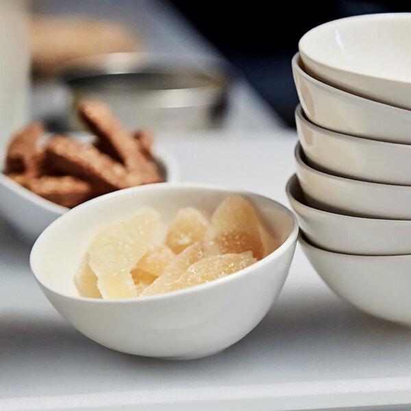 A close up of a stack of white bowls with a bowl of sugar on the counter.