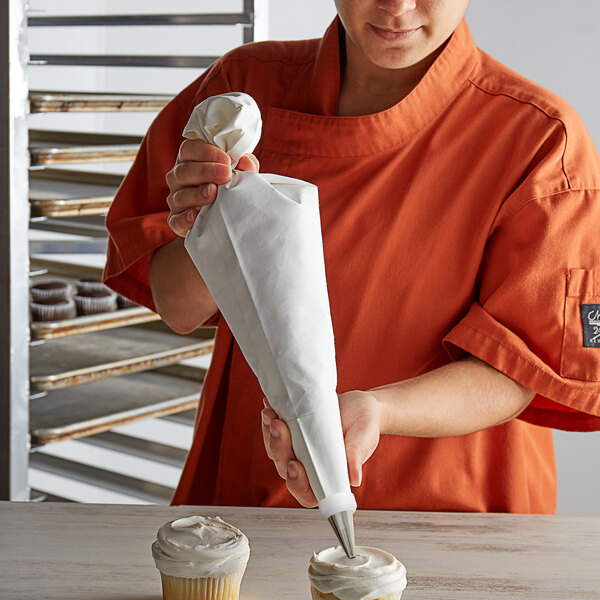 A person in an orange shirt using an Ateco polyurethane coated cotton pastry bag to frost a cupcake.