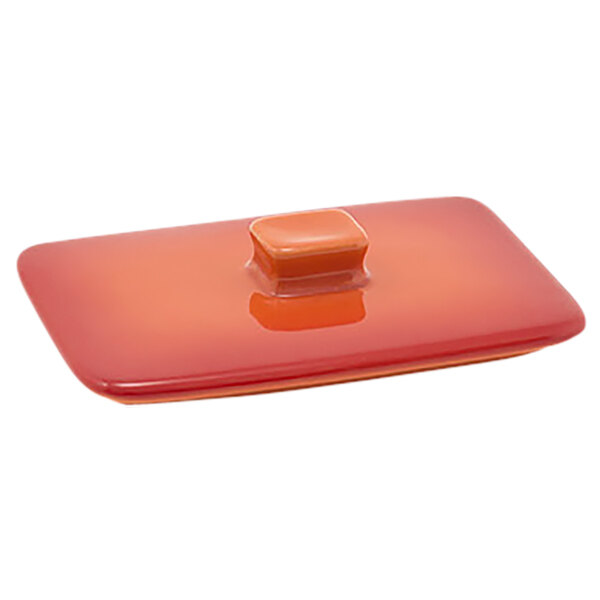 The front of a red rectangular stoneware lid with a square object on it.