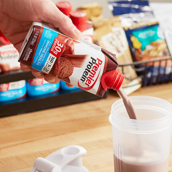 A hand pouring Premier Protein chocolate shake into a cup.