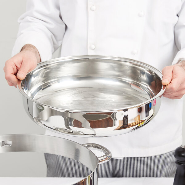 A chef holding a Vollrath stainless steel water pan.