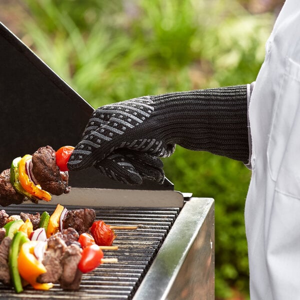 A person wearing Outset oven gloves cooking food on a grill.
