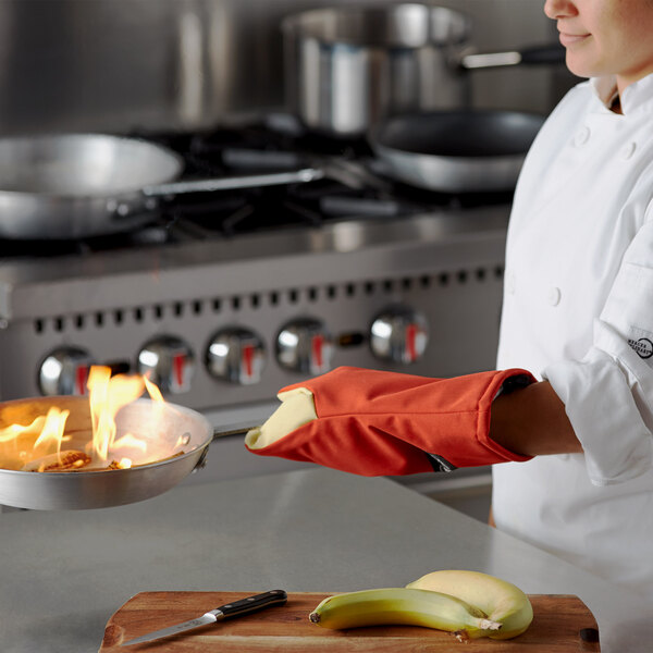 A chef in a white coat using a San Jamar Cool Touch Puppet Style Oven Mitt to hold a pan with fire in it.