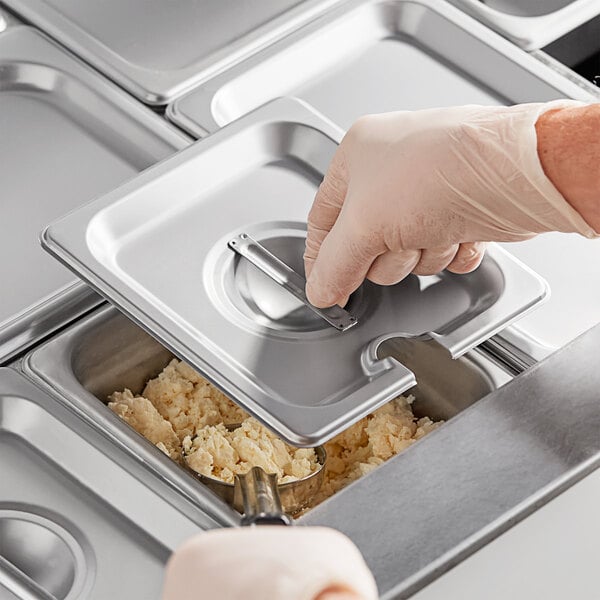 A person using a stainless steel slotted pan cover to remove food from a tray.