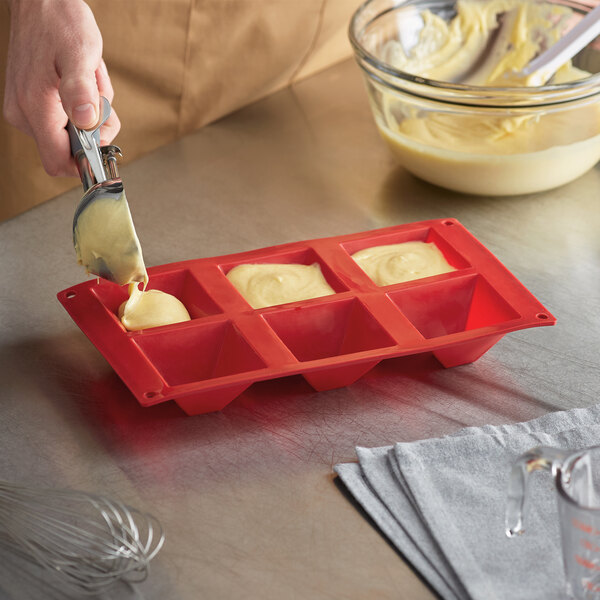 A person pouring yellow liquid into a red Thunder Group silicone mold.
