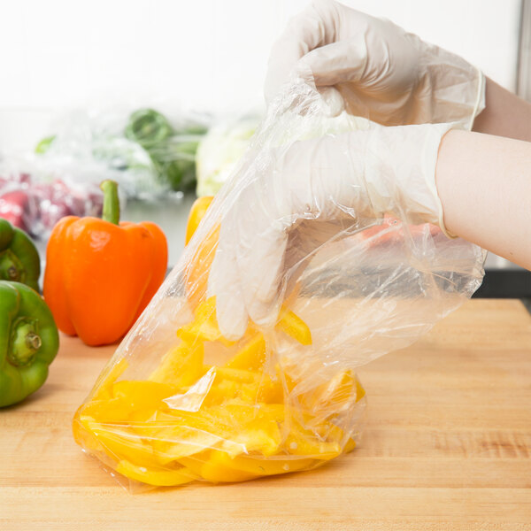 A person in gloves using a Inteplast Group plastic bag to hold yellow peppers.