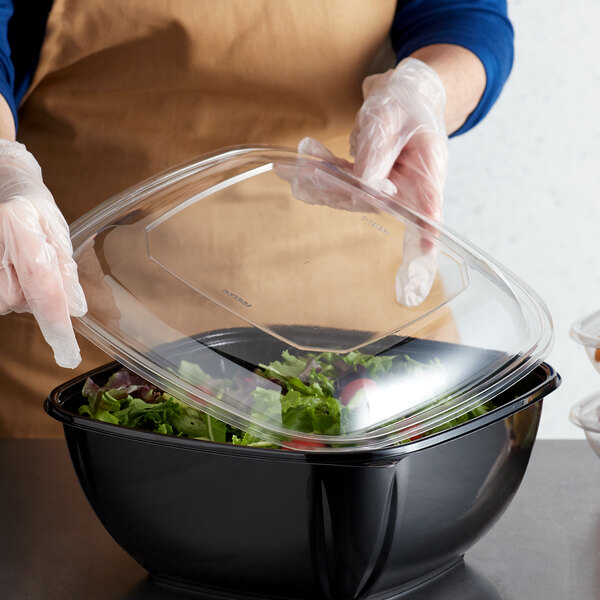A person putting a Fineline clear plastic lid on a salad in a plastic container.
