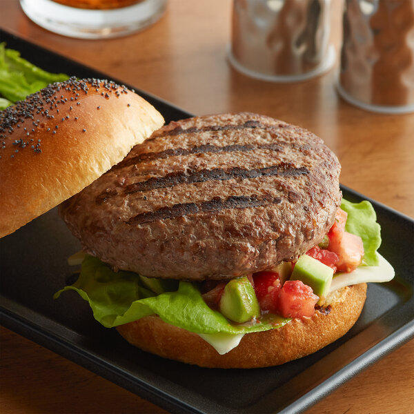 A Warrington Farm Meats burger with lettuce and tomato on a black plate.