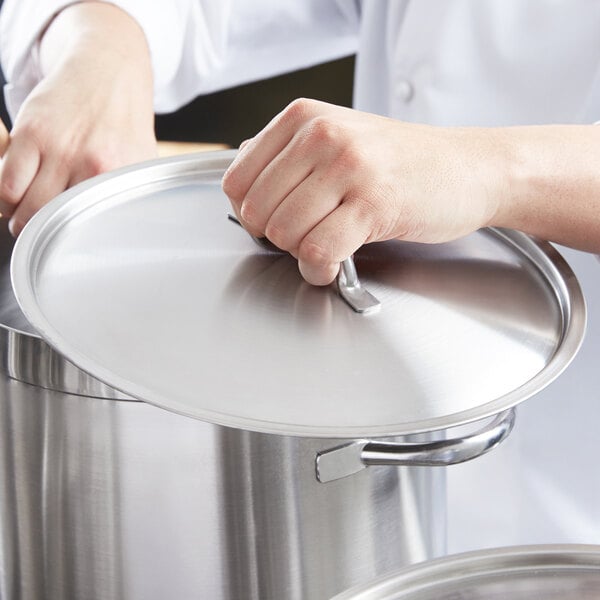 A person holding a Vollrath stainless steel domed cover over a silver pot.