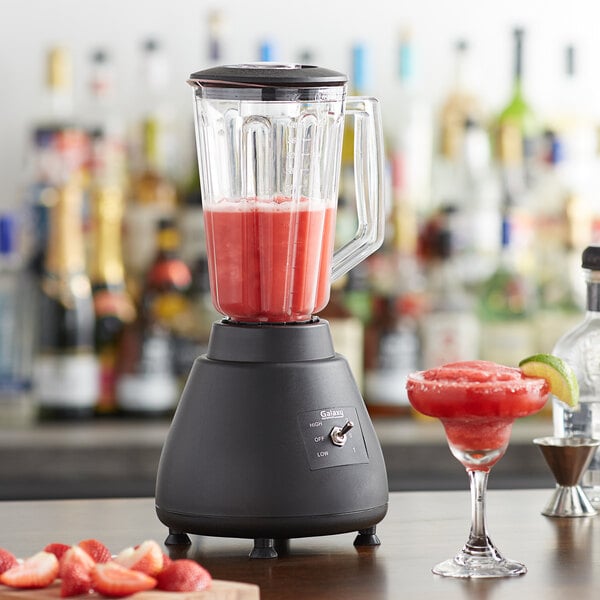 A Galaxy bar blender with a red strawberry drink in a glass on a table.