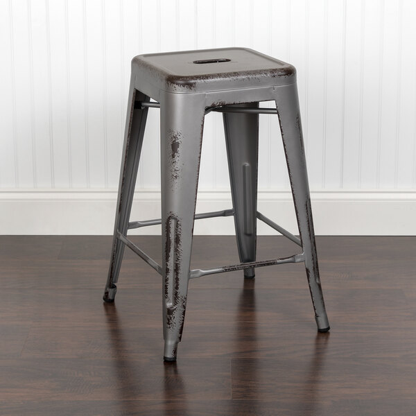 A Flash Furniture distressed silver metal counter height stool with a drain hole seat on a wood floor.