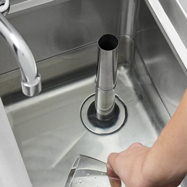 A hand holding a glass in a sink with a stainless steel overflow pipe attached to the drain.