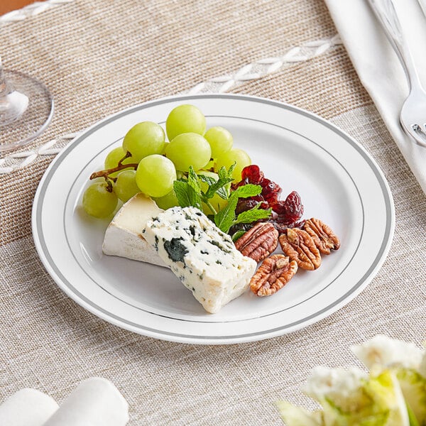 A Visions white plastic plate with silver bands holding grapes and nuts on a table.