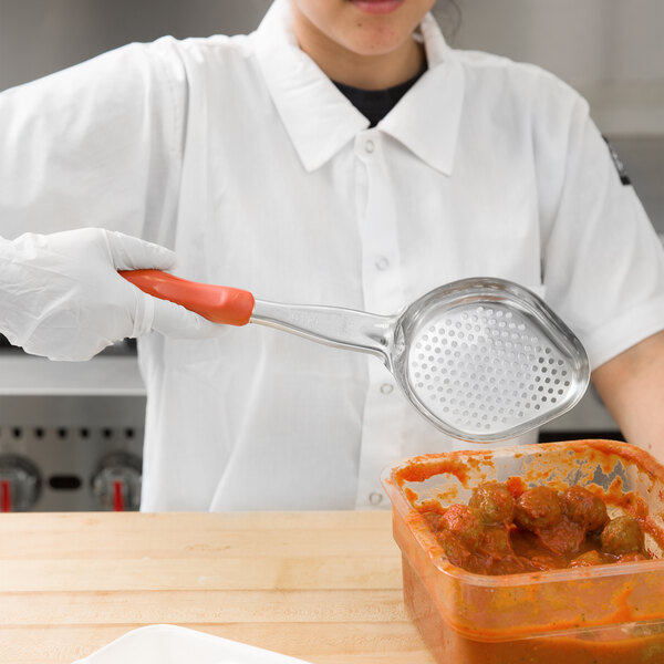 A woman in a white coat using a Vollrath Orange Perforated Oval Spoodle to pour sauce into a container of food.