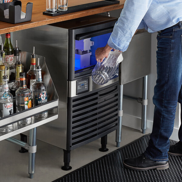 A man pouring a drink from a clear glass pitcher into an Avantco undercounter full cube ice machine.