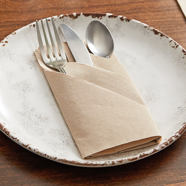 A plate with a Hoffmaster FashnPoint natural dinner napkin and silverware on it.
