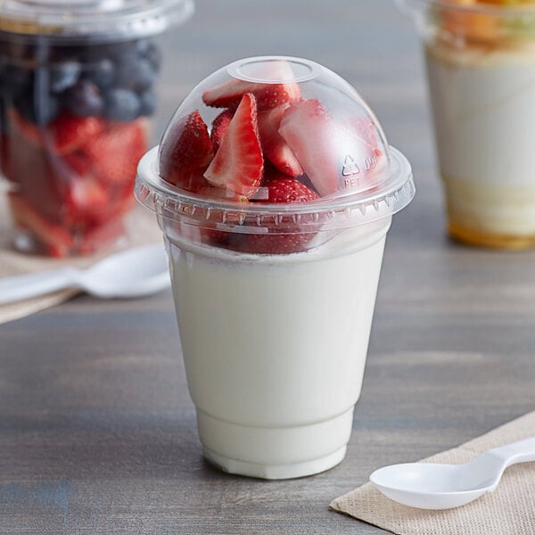 A Choice clear plastic cup of yogurt with strawberries and blueberries on a white table.
