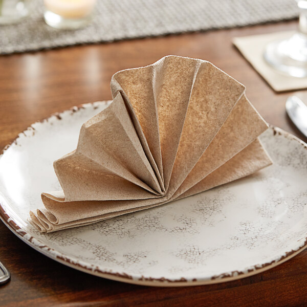 A white plate with a folded Hoffmaster Linen-Like Natural dinner napkin on it.