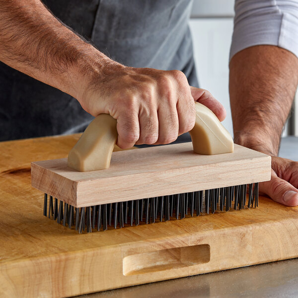 A person using a Carlisle wooden butcher block brush to clean a wooden cutting board.