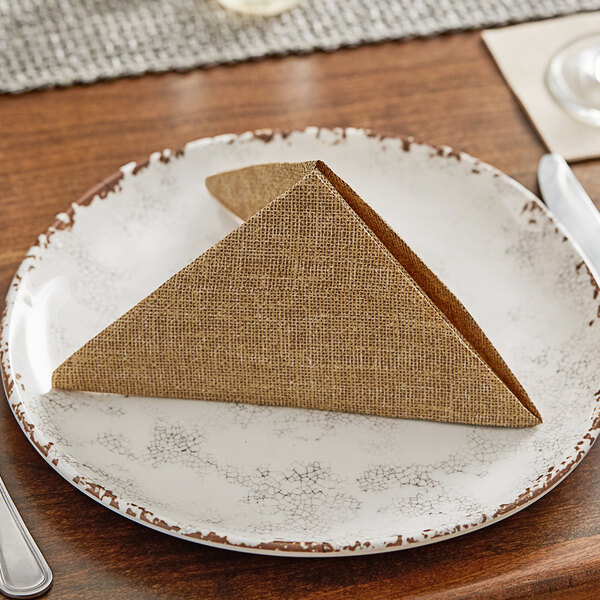A folded Hoffmaster FashnPoint burlap print dinner napkin on a white plate.