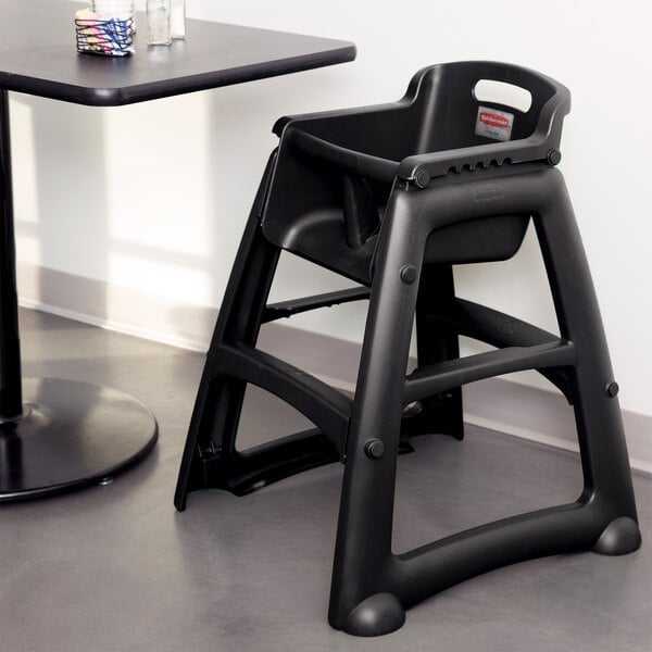 A black Rubbermaid high chair sits next to a table.