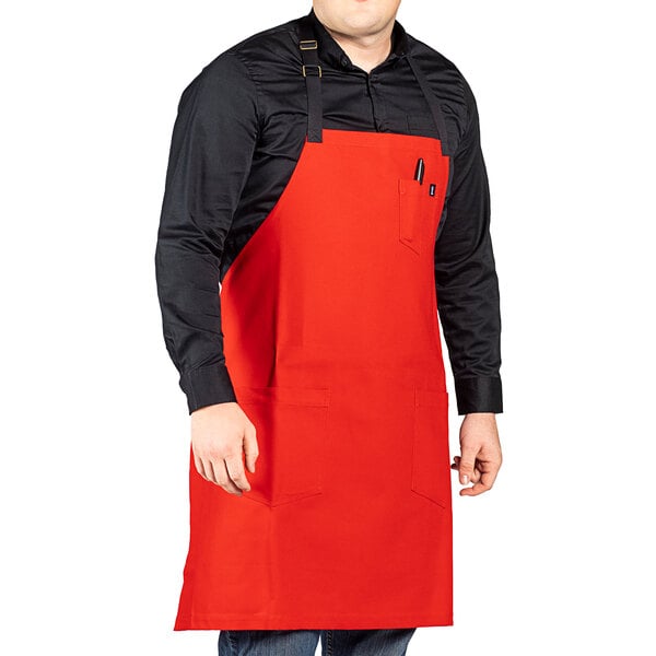A man wearing a red Uncommon Chef aura bib apron with black webbing.