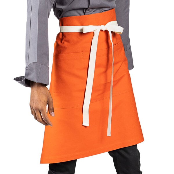 An orange Uncommon Chef Moxie waist apron with white webbing on the pockets.