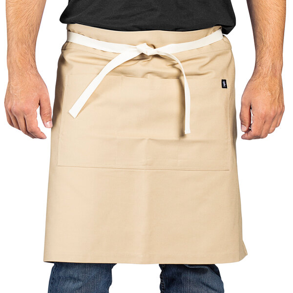 A man wearing a light beige Uncommon Chef Moxie waist apron with natural webbing.